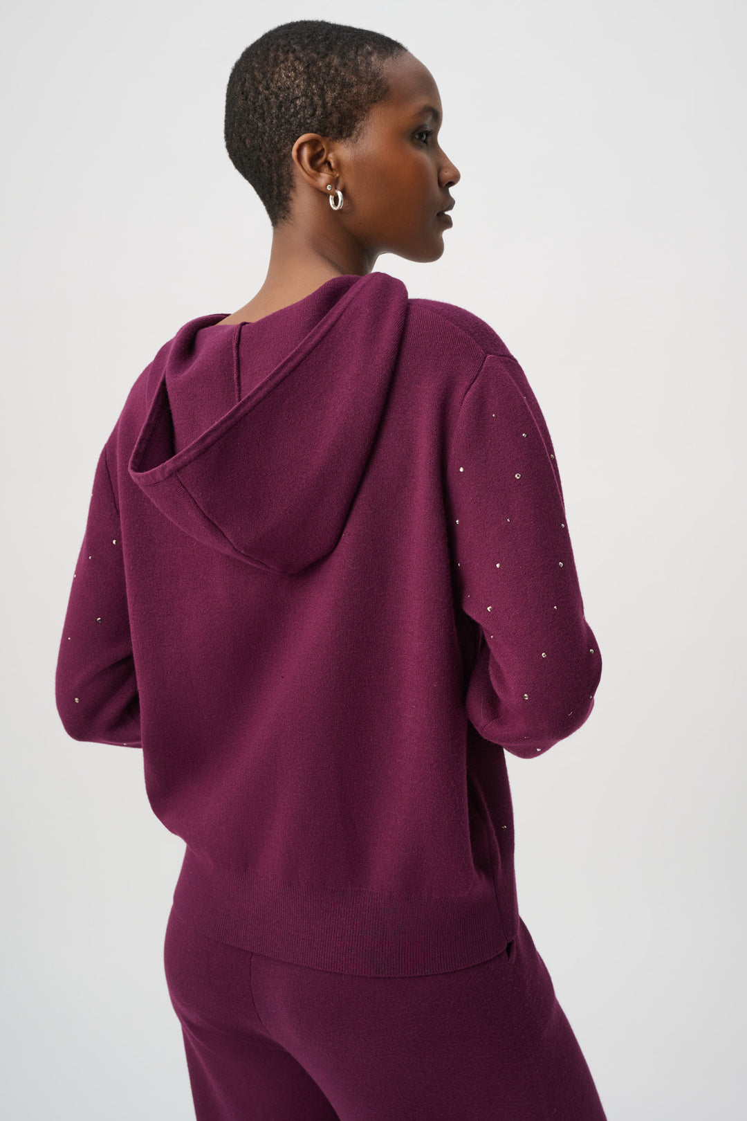Person wearing a maroon hoodie with decorative elements on a white background