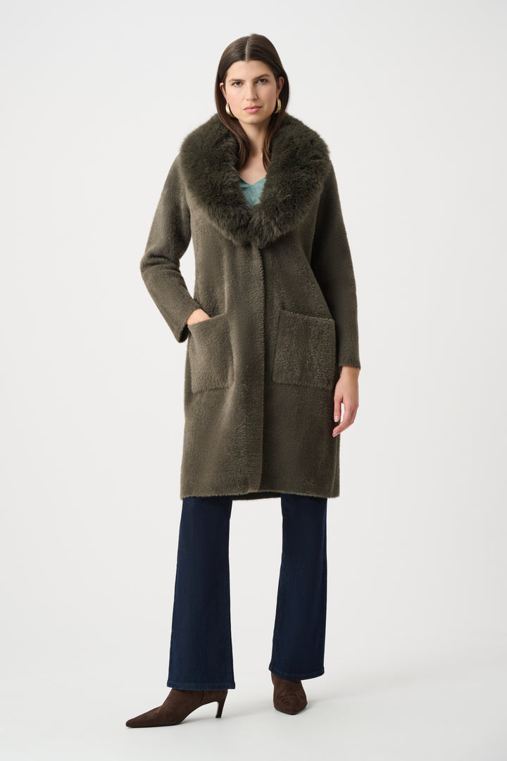 Woman wearing a long olive green coat with fur collar on a white background