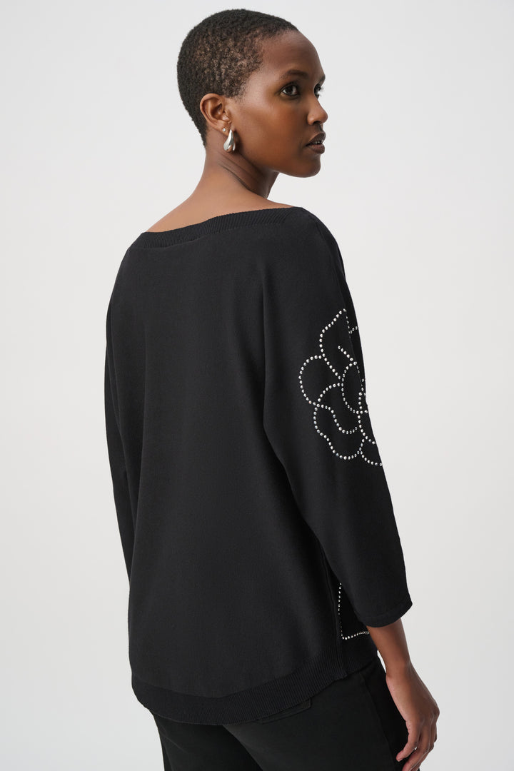 A woman shown from the back wearing a black top with floral embellishments on a white background
