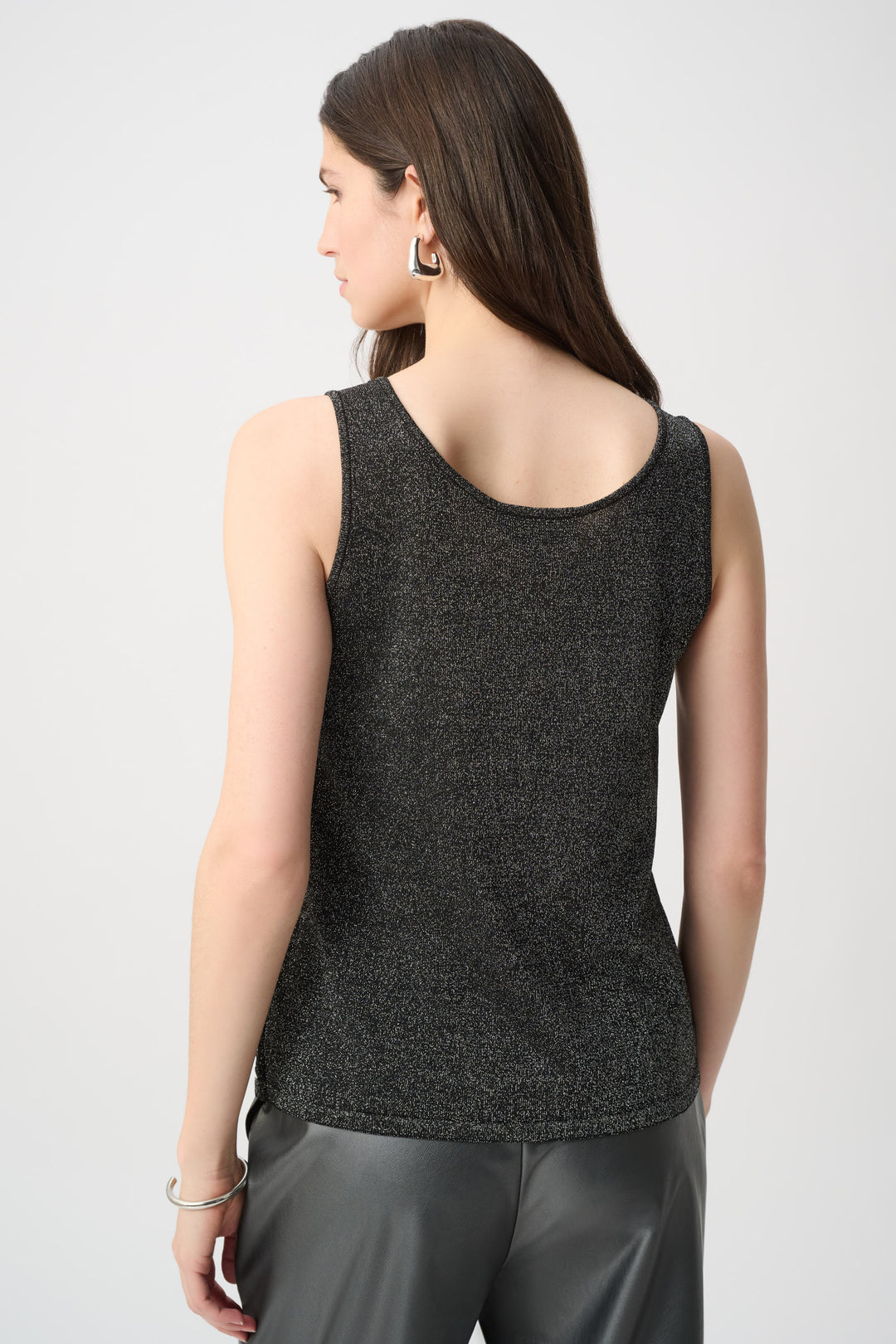 A woman shown from the back wearing a black camisole with crochet rhinestone details on the front and a sparkly back, dark silver leather pants on a white background. 