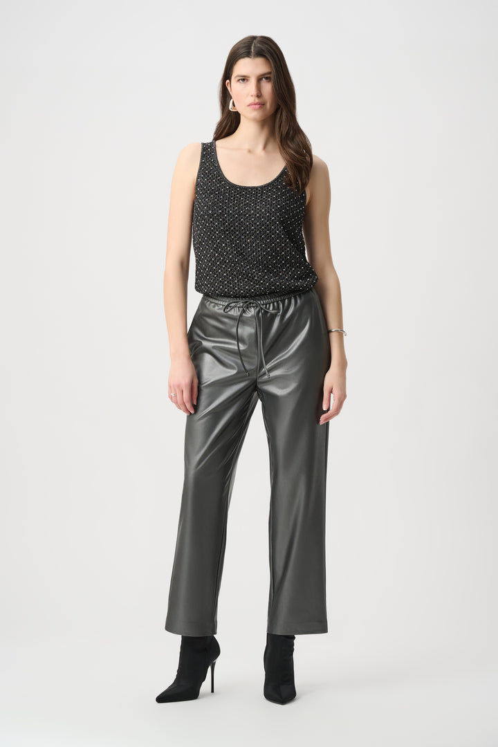 A woman wearing a black camisole with crochet rhinestone details on the front, dark silver leather pants on a white background. 