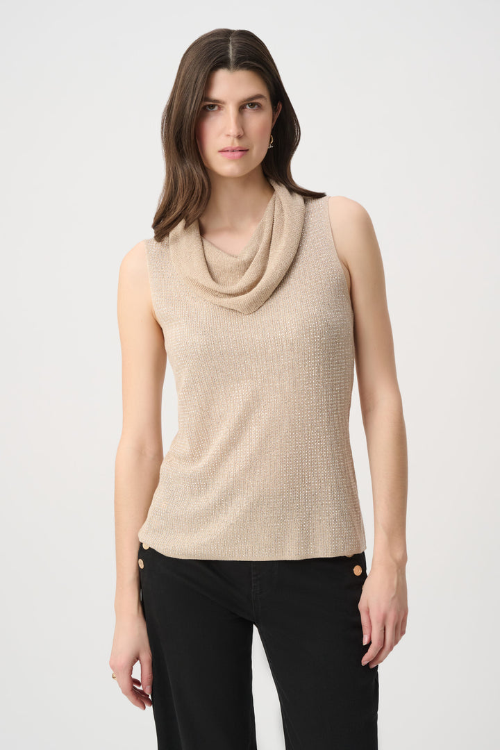 A woman wearing a shimmery gold cowl neck sleeveless top and black pants in front of a white background. 