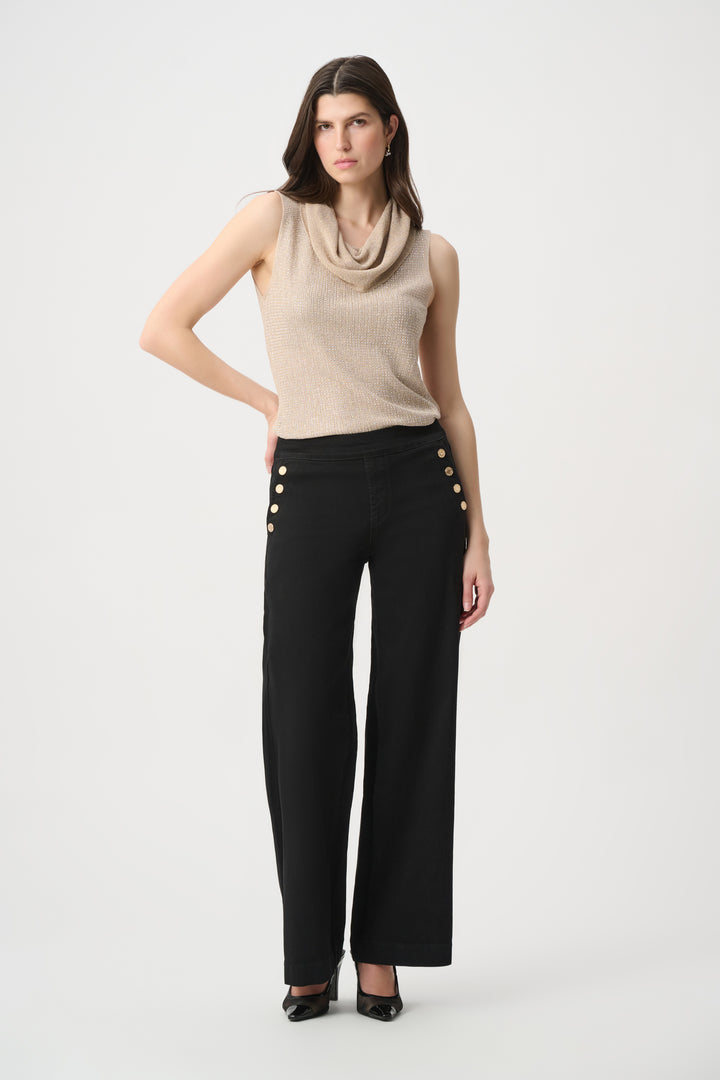A woman wearing a shimmery gold cowl neck sleeveless top and black pants in front of a white background. 
