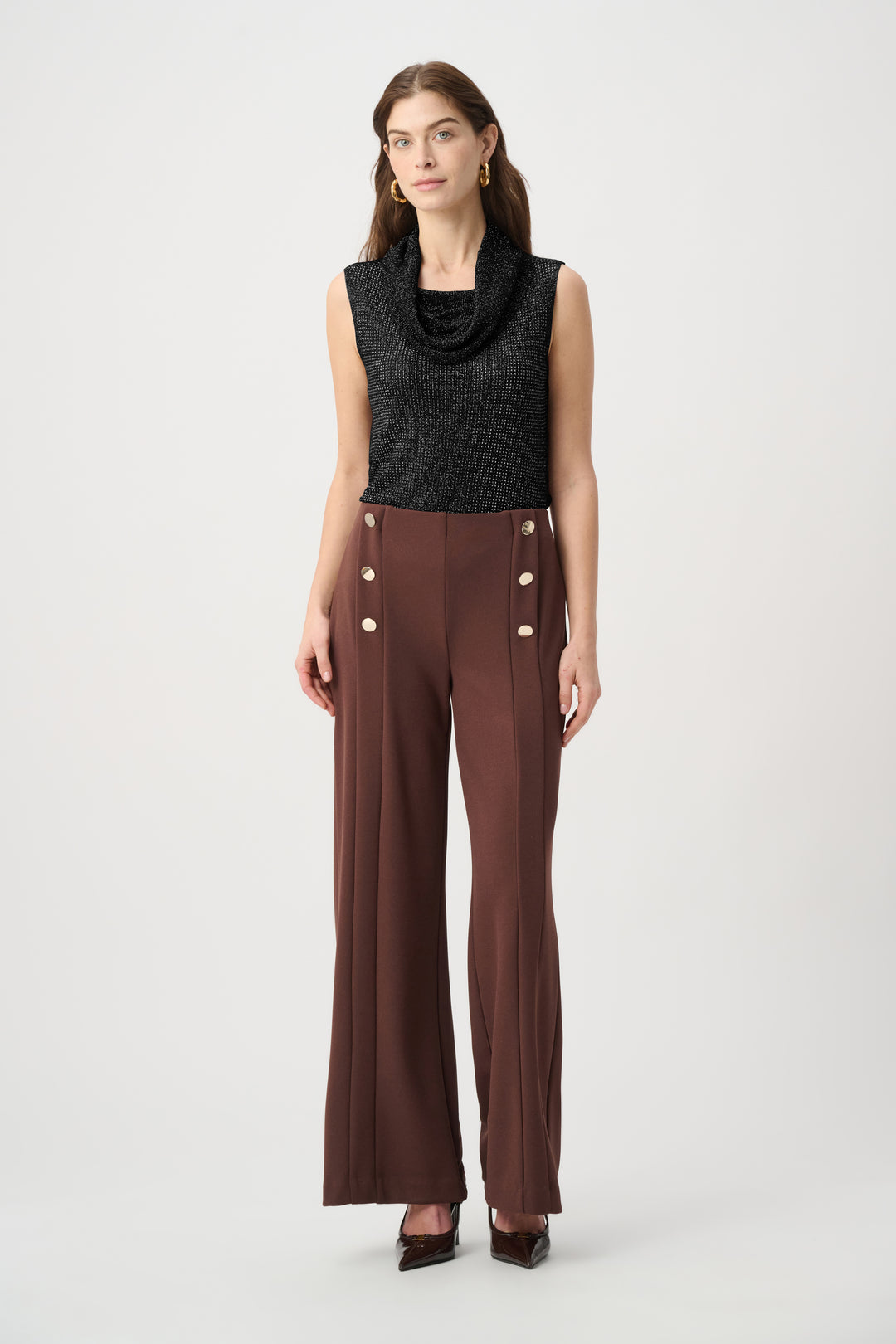 Woman wearing a black sleeveless top and brown pants with button details on a white background