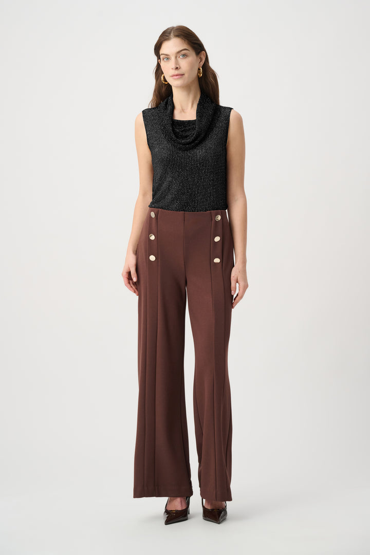 Woman wearing a black sleeveless top and brown pants with button details on a white background