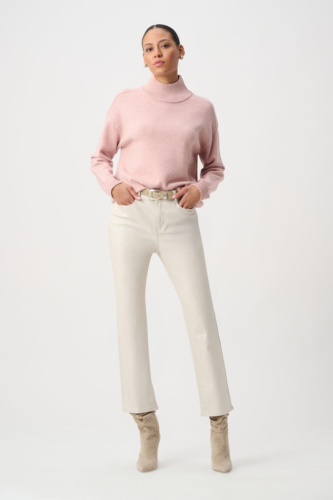 Woman wearing a pink turtleneck sweater, white pants, and beige boots on a white background