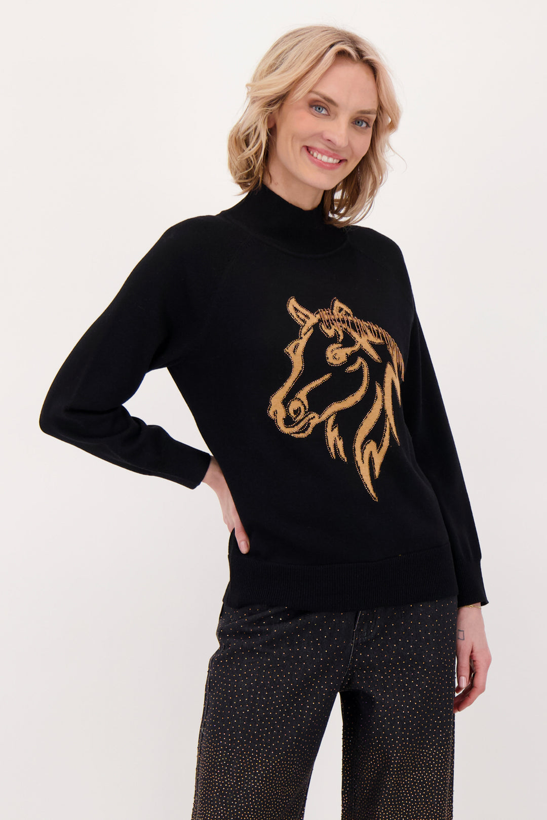 A woman modelling a black sweater with beaded horse head in front of a white background. 