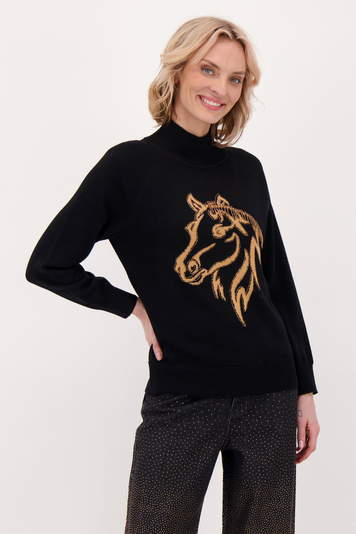 A woman modelling a black sweater with beaded horse head in front of a white background. 