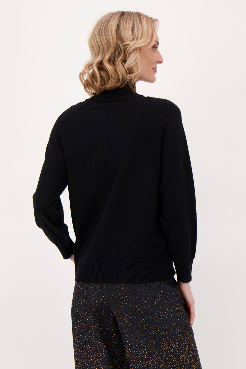 A woman modelling a black sweater with beaded horse head in front of a white background. 