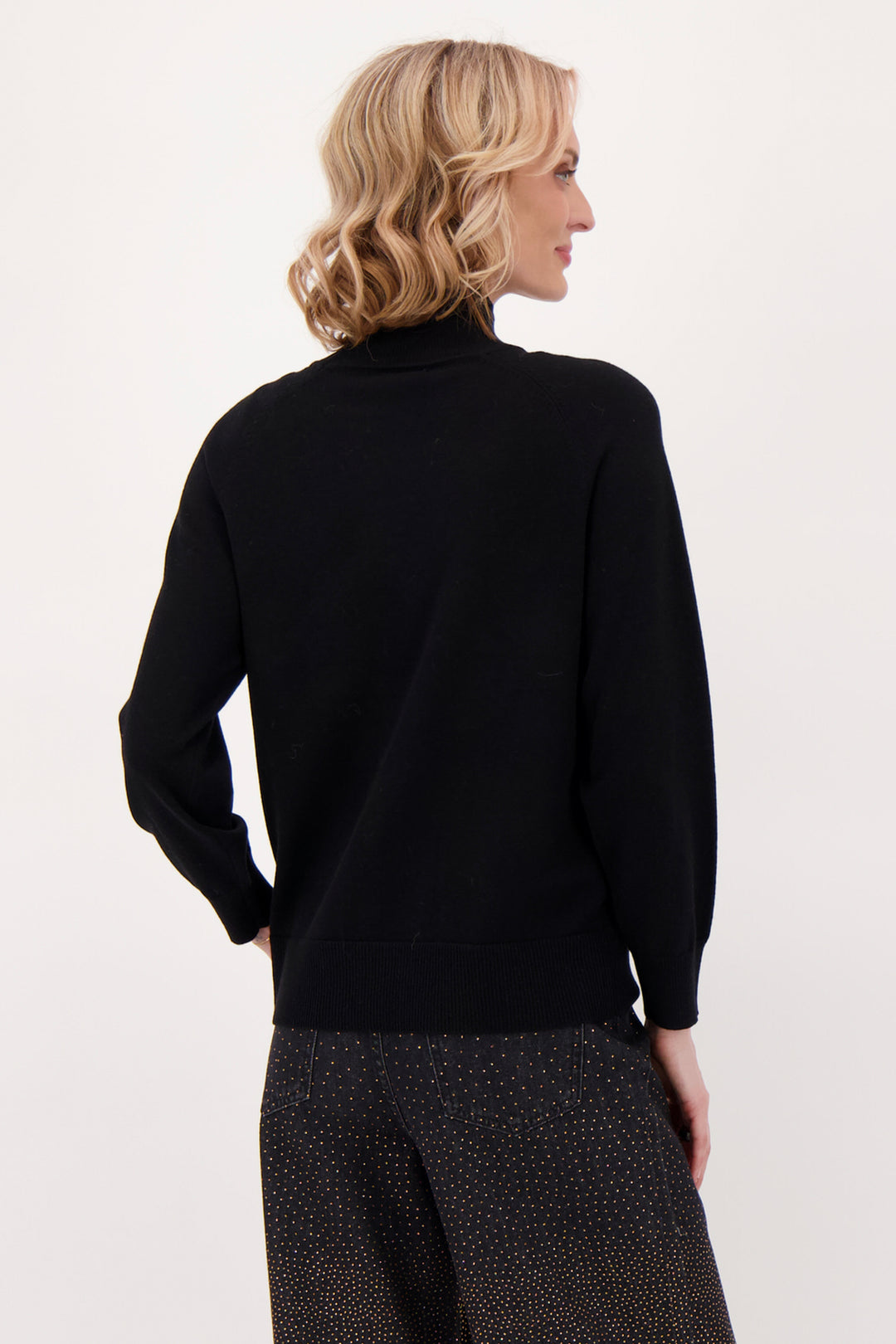 A woman modelling a black sweater with beaded horse head in front of a white background. 