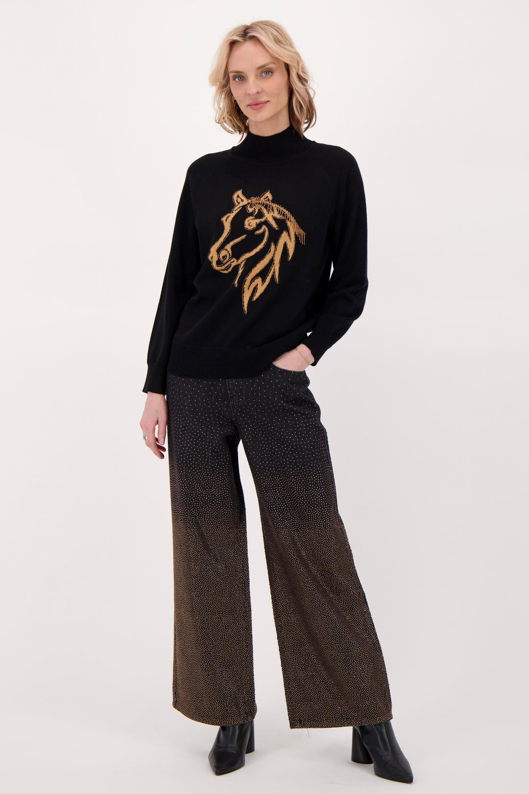 A woman modelling a black sweater with beaded horse head in front of a white background. 