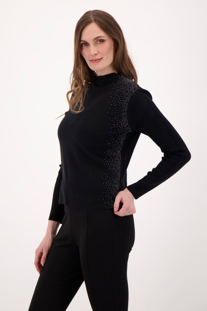 A woman modelling a black sweater with rhinestone embellishments in front of a light grey background. 
