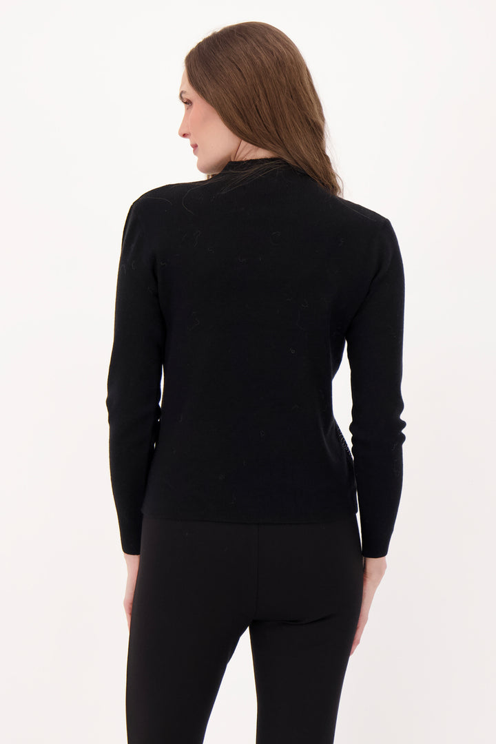 A woman modelling a black sweater with rhinestone embellishments in front of a light grey background. 