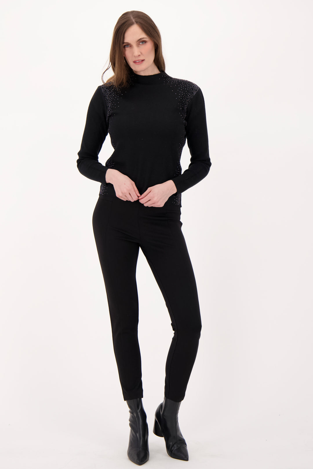 A woman modelling a black sweater with rhinestone embellishments in front of a light grey background. 
