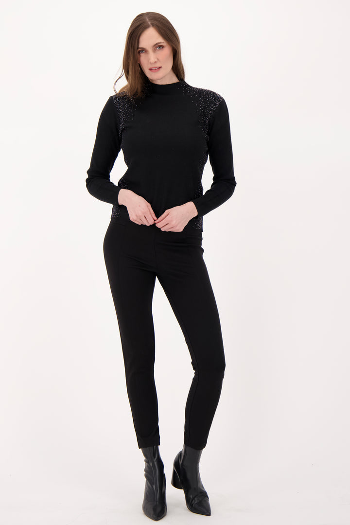 A woman modelling a black sweater with rhinestone embellishments in front of a light grey background. 