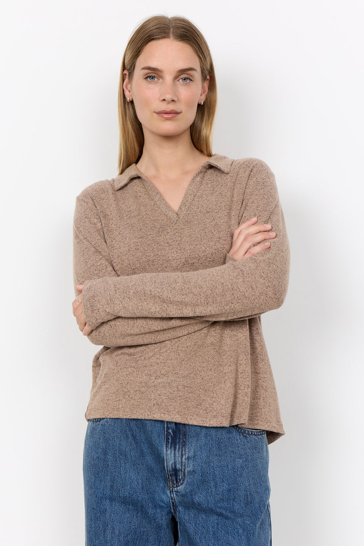 A woman modelling a long sleeve polo sweater and jeans in front of a white background. 