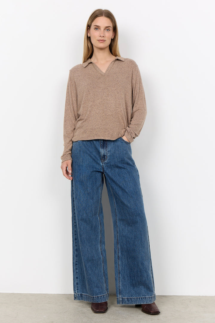 A woman modelling a long sleeve polo sweater and jeans in front of a white background. 