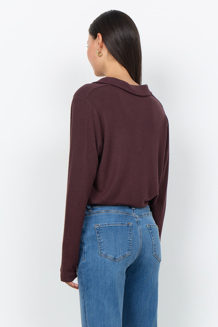 A woman modelling a long sleeve polo sweater and jeans in front of a white background. 