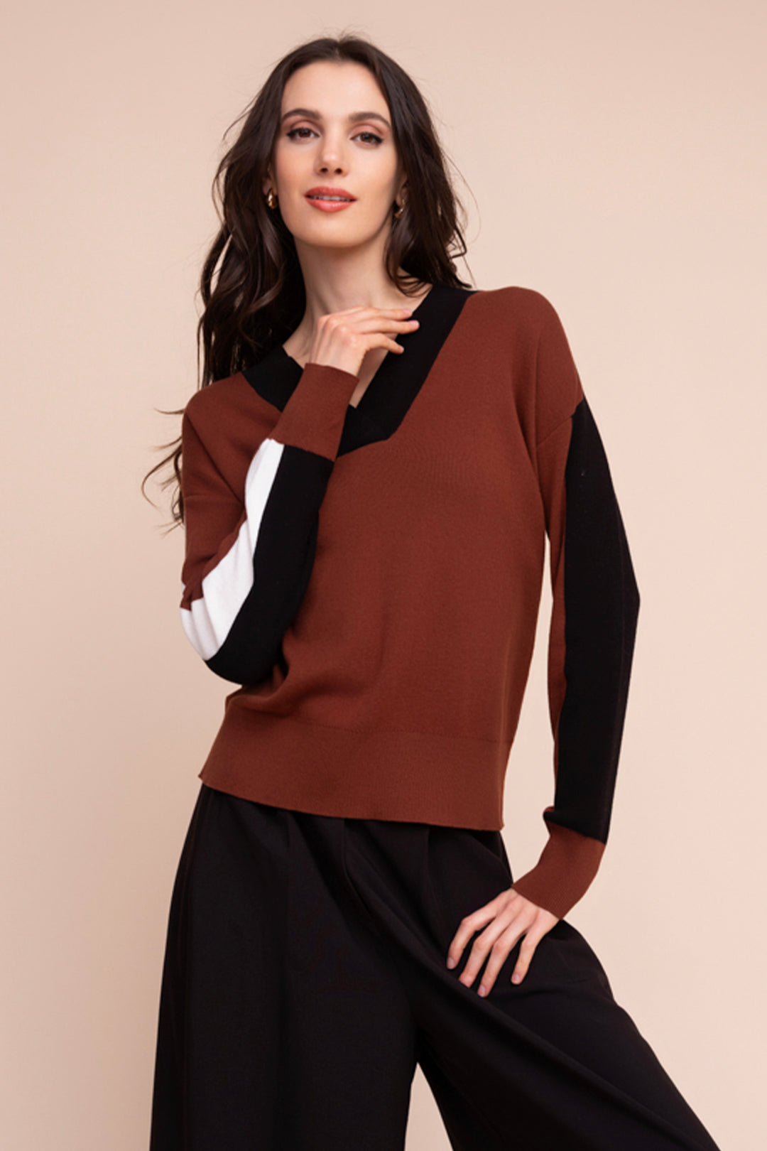 A woman modelling a brown colourblock sweater in front of a beige background. 