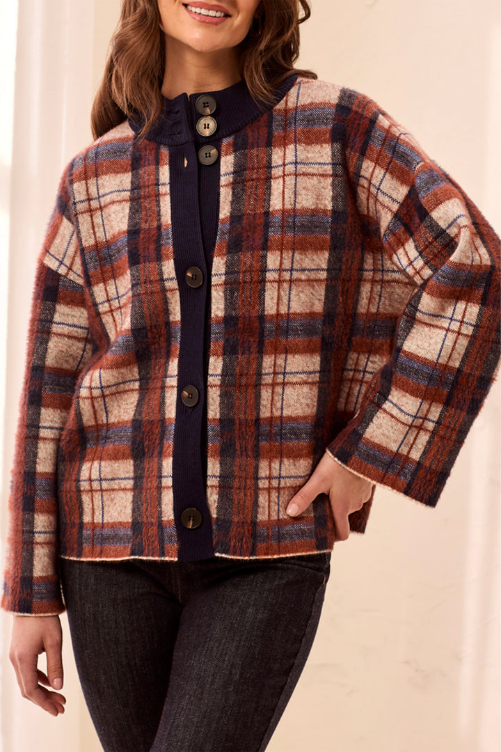 A woman modelling a plaid boxy cardigan in front of a beige background. 