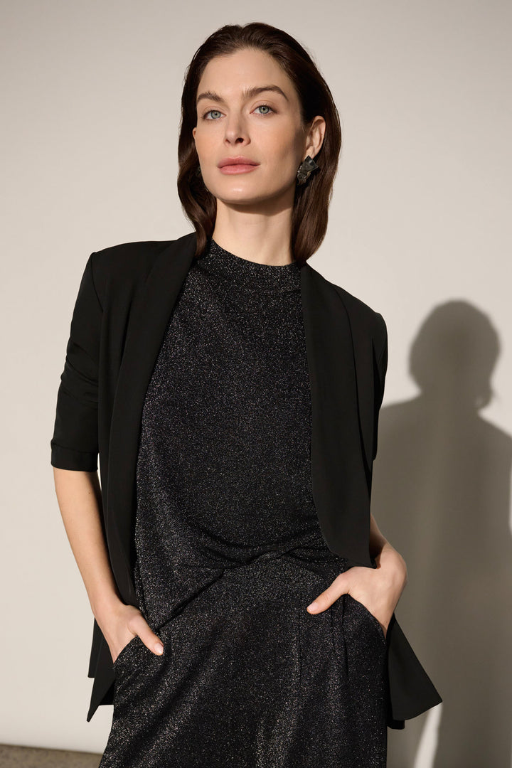 A woman modelling a black shimmery t-shirt top with a mock neck and matching pants.