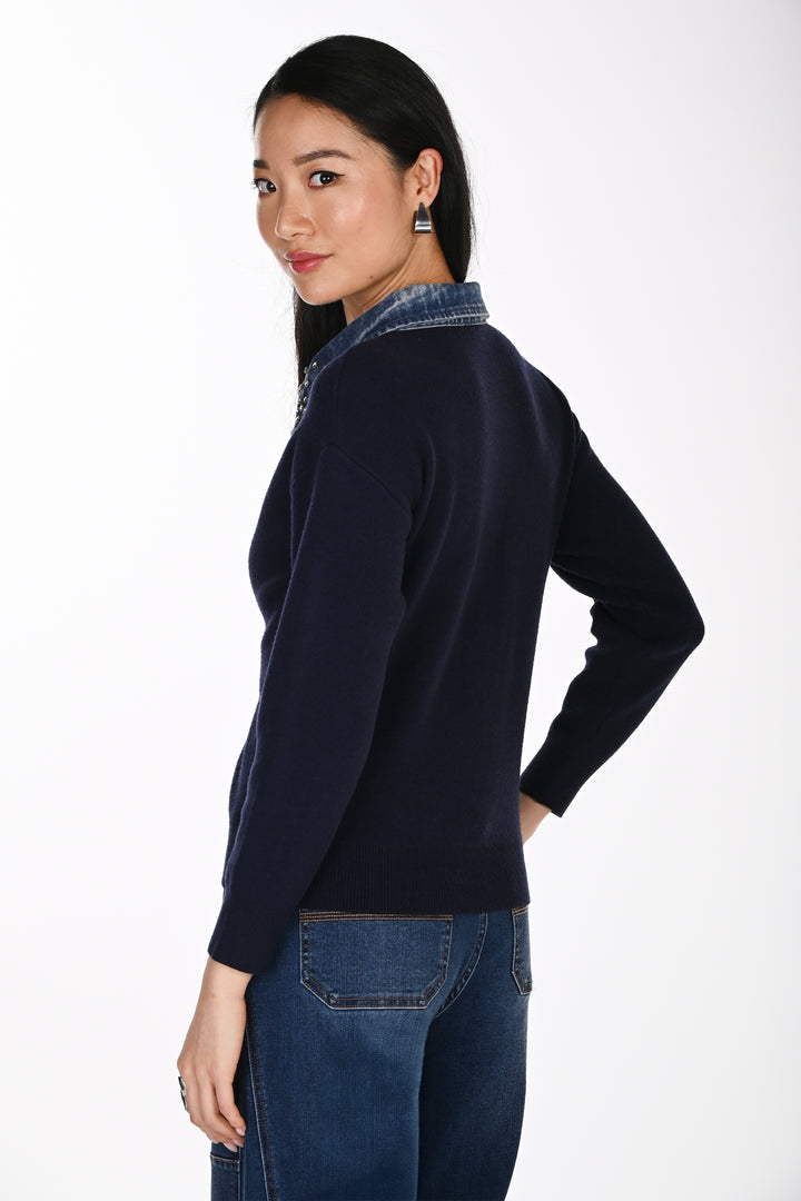 A woman shown from the back modelling a navy sweater with a denim and rhinestone collar standing in front of a white background. 