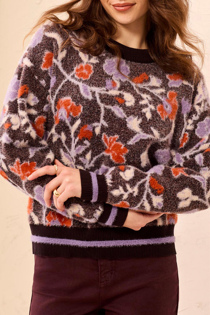 A woman modelling a long sleeve sweater with floral pattern standing in front of a light beige background. 