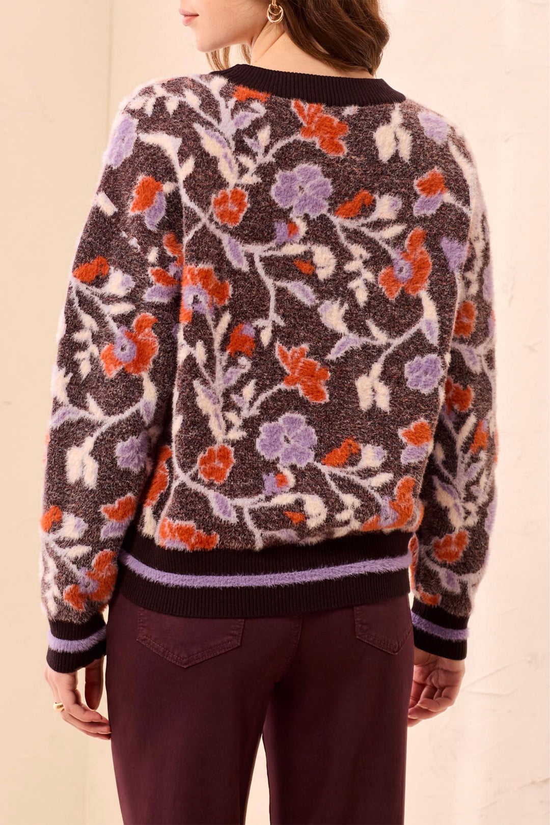 A woman shown from the back modelling a long sleeve sweater with floral pattern standing in front of a light beige background. 