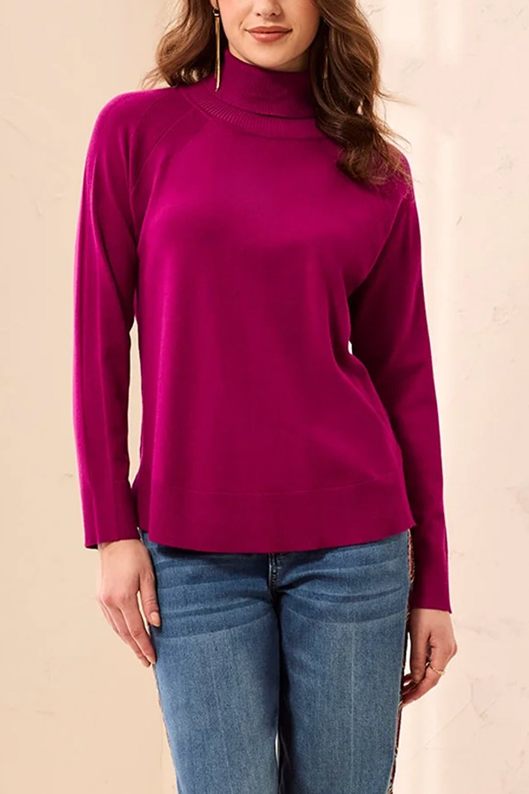 A woman shown from the back modelling a long sleeve magenta turtleneck sweater and jeans standing in front of a light beige background. 