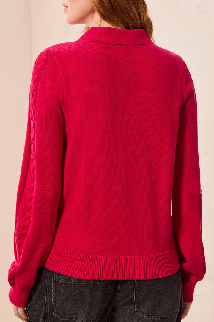 A woman shown from the back modelling a polo style long sleeve sweater with cable knit details up the sleeves. She is standing in front of a light beige background. 