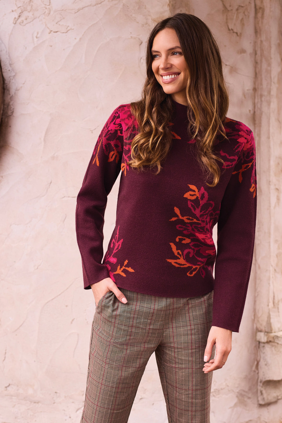 A woman shown from the back modelling a deep brown long sleeve sweater, with a mock neck and floral details.