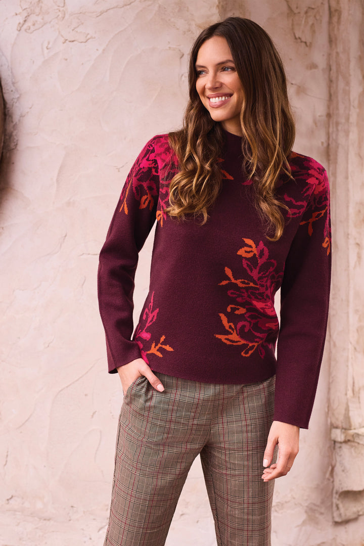 A woman shown from the back modelling a deep brown long sleeve sweater, with a mock neck and floral details.