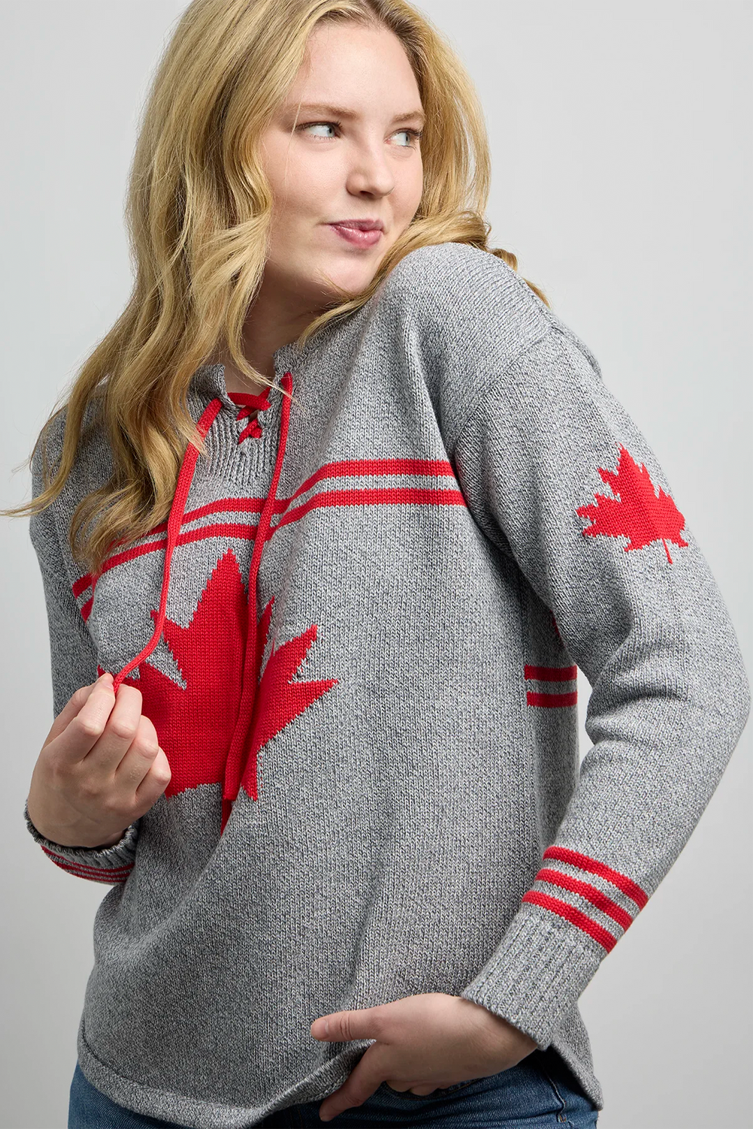 A woman modelling a grey hockey jersey style sweater with a large maple leaf on the front, maple leaf on the sleeve and Canada across the back. 