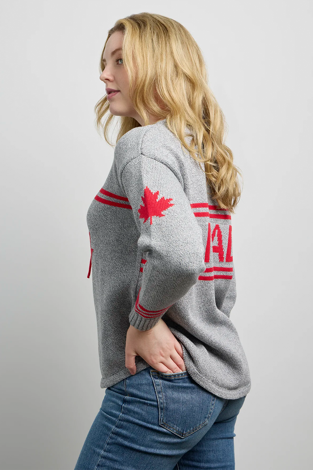 A woman modelling a grey hockey jersey style sweater with a large maple leaf on the front, maple leaf on the sleeve and Canada across the back. 