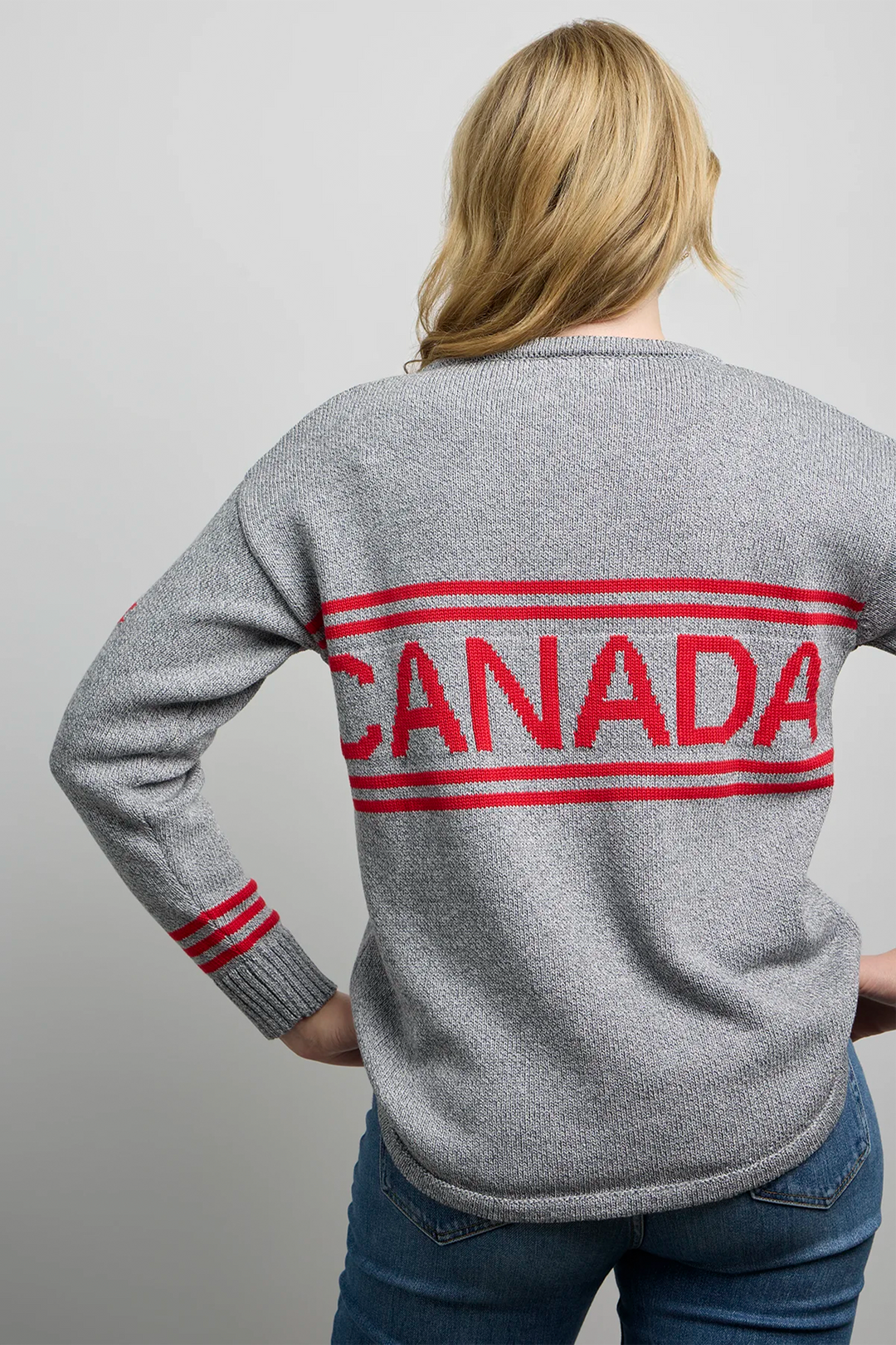 A woman modelling a grey hockey jersey style sweater with a large maple leaf on the front, maple leaf on the sleeve and Canada across the back. 