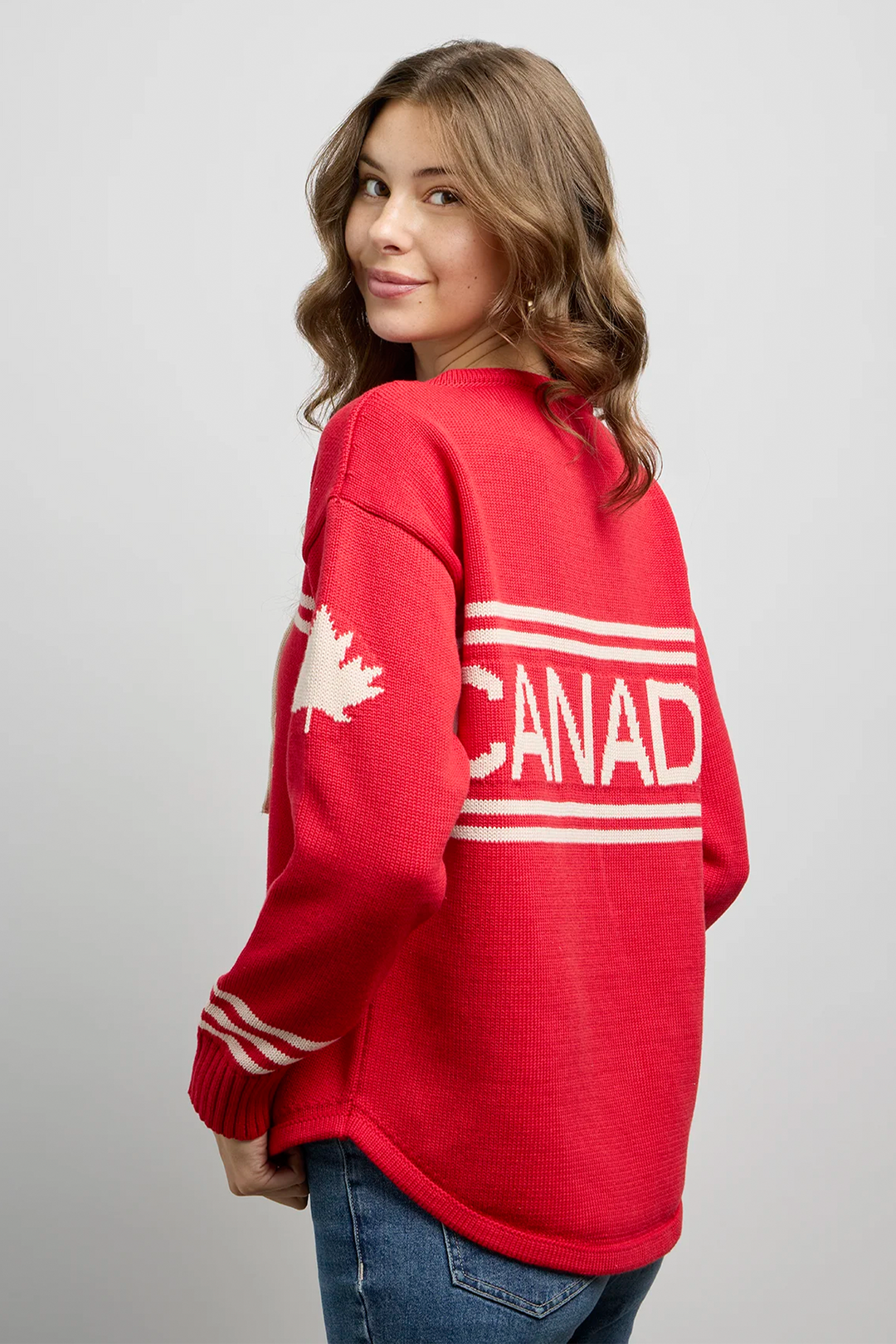 A woman modelling a red hockey jersey style sweater with a maple leaf on the sleeve and Canada across the back. 