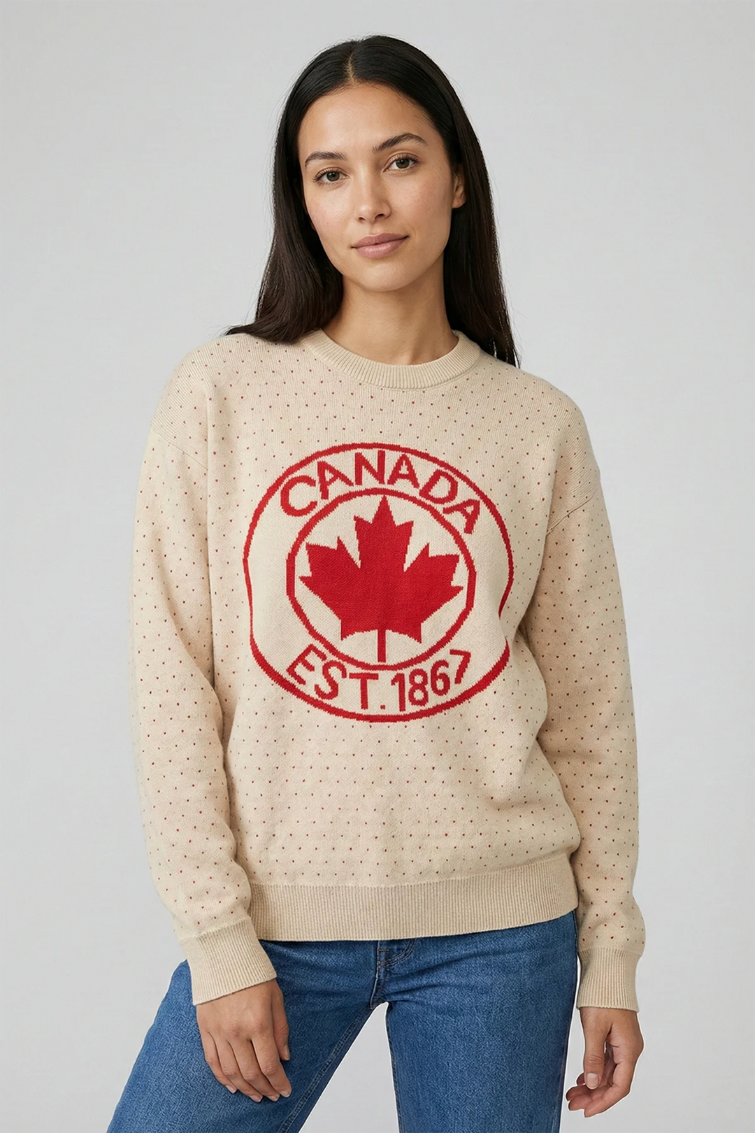 A woman modelling a beige sweater with red polka dots and a maple leaf and Canada est. 1867 written in a circle on the front. 