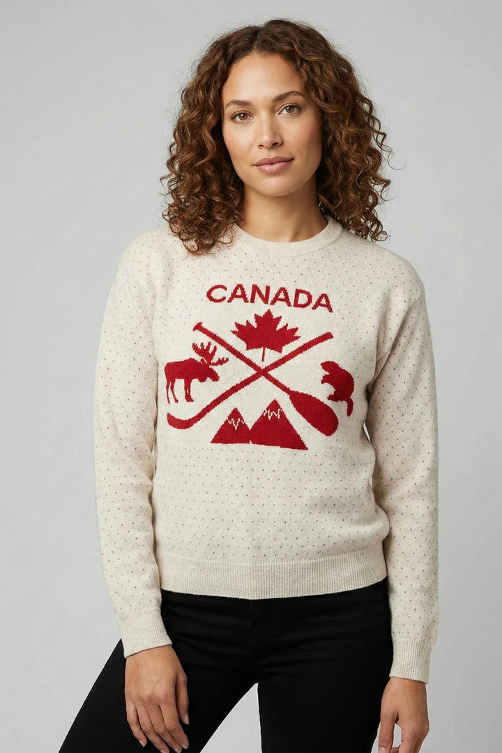 A woman modelling a beige sweater with red polka dots and a large Canada, maple leaf, mountain, bever and moose graphics on the front. 