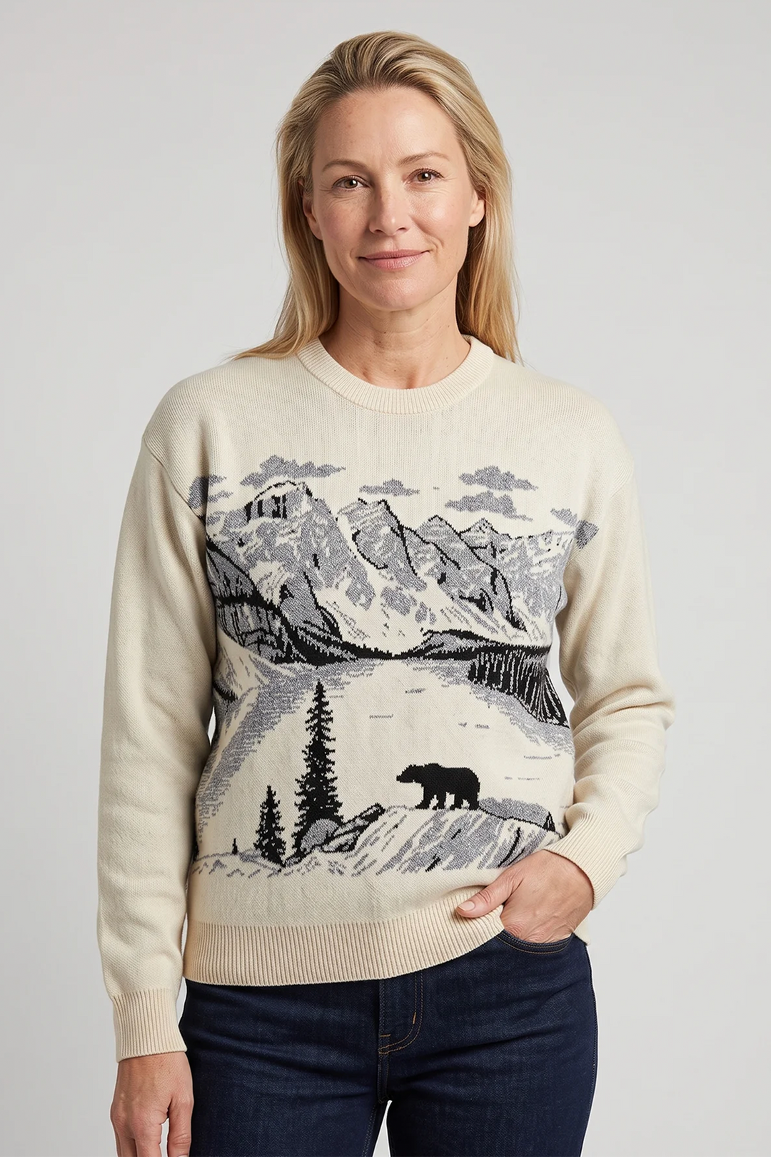 A woman wearing a beige long sleeve sweater with a beautiful grey mountain and bear landscape scene on the front. 