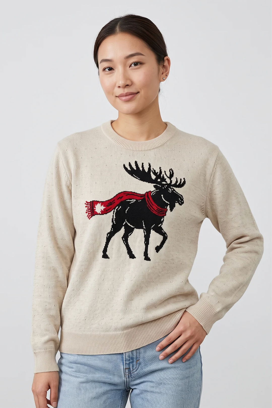 A woman wearing a beige long sleeve sweater with a black moose graphic on the front. The moose is wearing a red maple leaf scarf. 