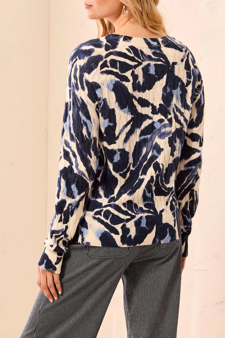A woman shown from the back wearing a beige sweater with navy and blue floral details standing in front of a beige background. 
