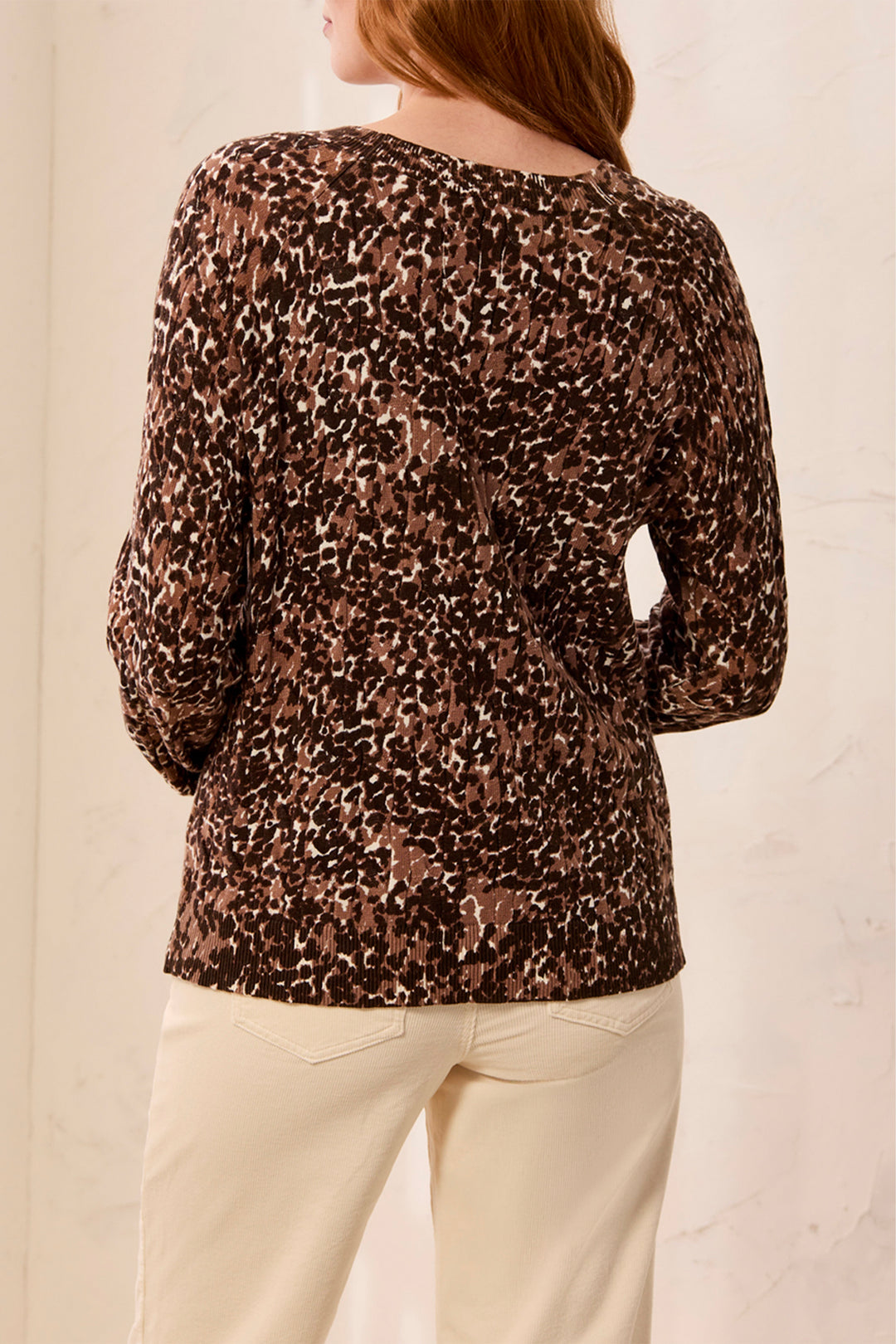 A woman shown from the back wearing a brown animal print ,long sleeve sweater standing in front of a beige background. 