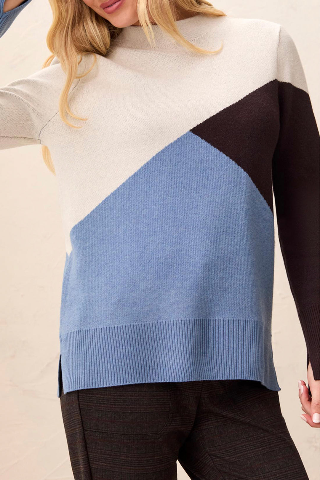 A woman wearing a colourblock long sleeve sweater standing in front of a beige background. 
