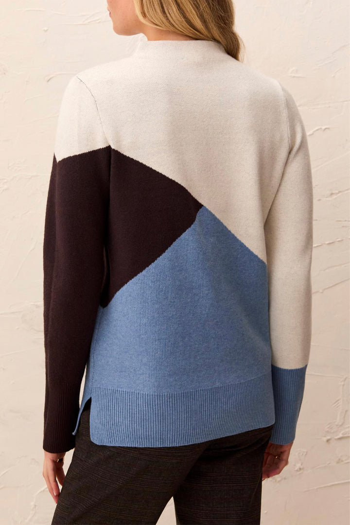 A woman shown from the back wearing a colourblock long sleeve sweater standing in front of a beige background. 