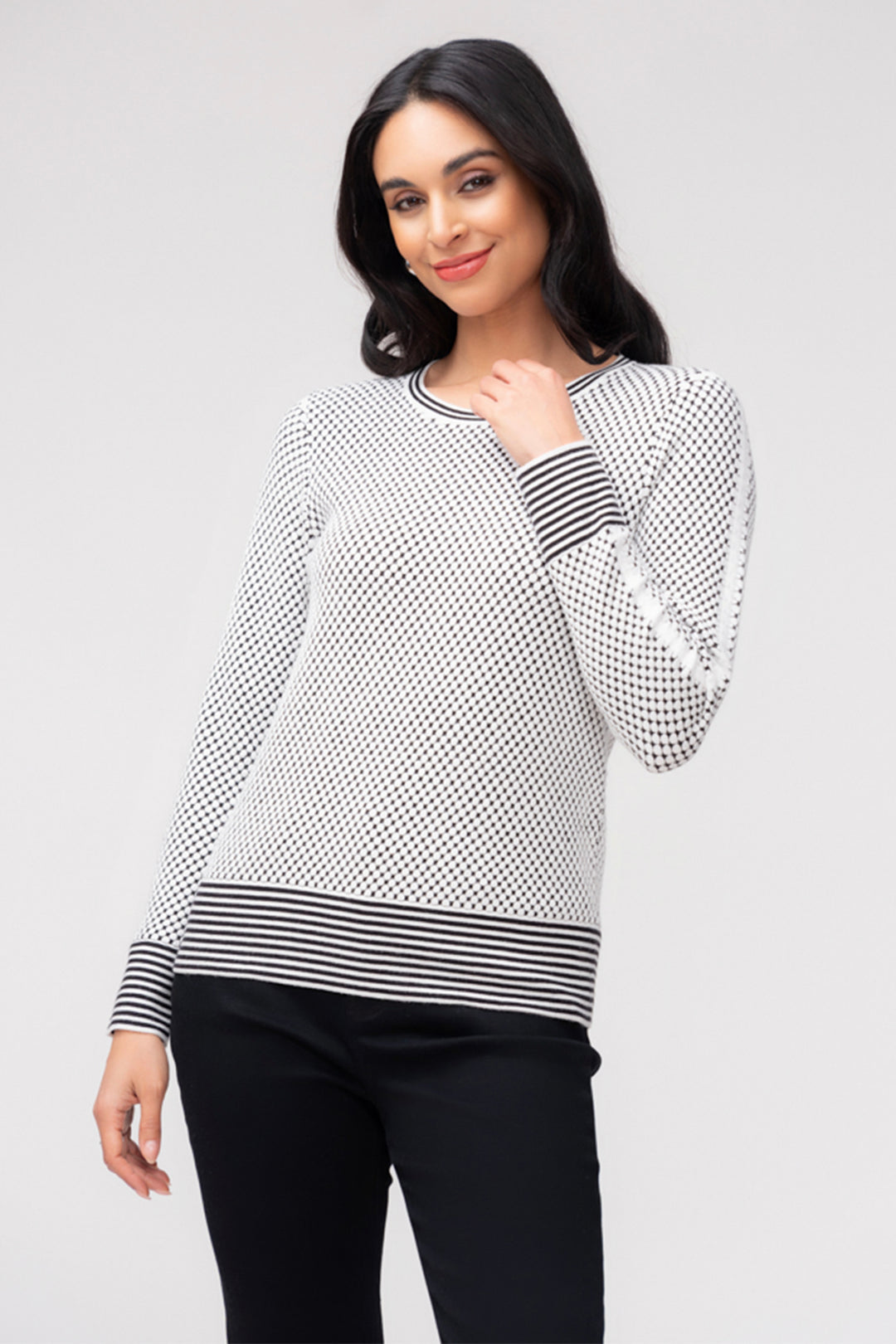 A woman wearing a long sleeve waffle dot print with removable scarf. She is wearing black pants and standing in front of a light grey background. 