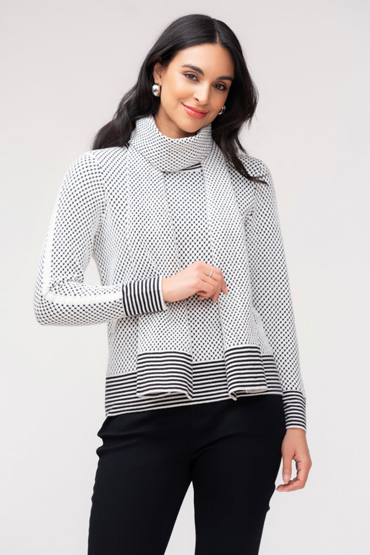 A woman wearing a long sleeve waffle dot print with removable scarf. She is wearing black pants and standing in front of a light grey background. 