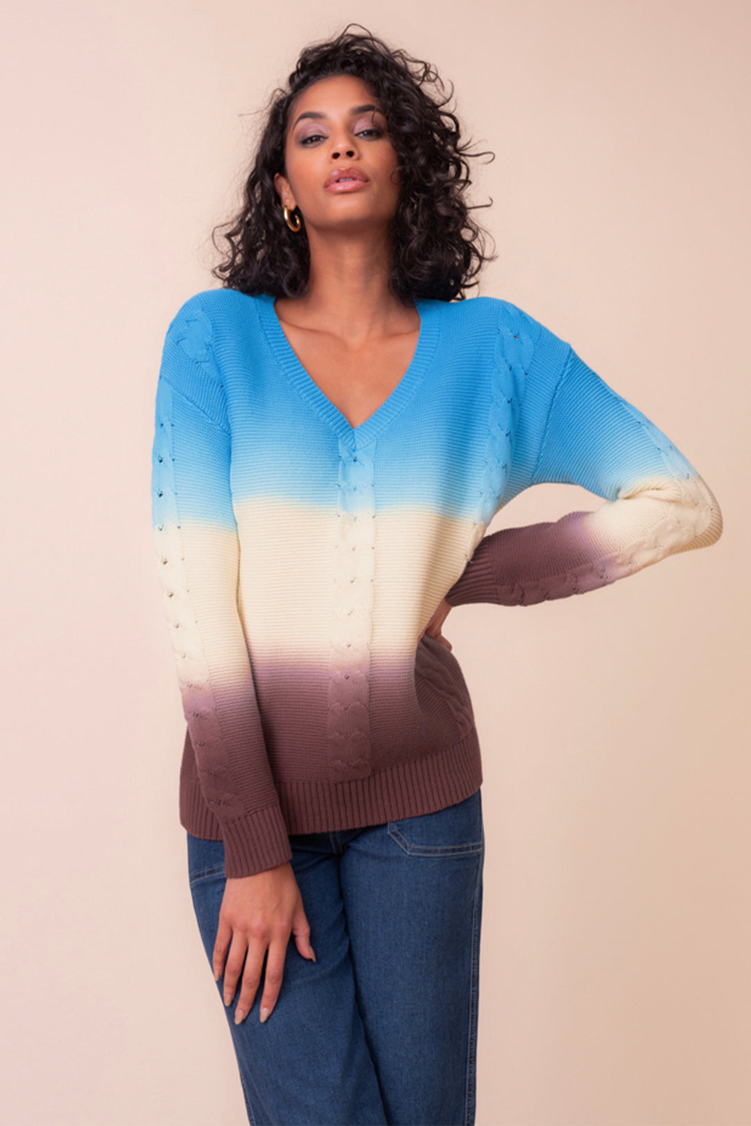 A woman wearing an ombre effect cable knit long sleeve sweater standing in front of a beige background. 