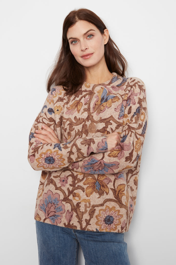 A woman wearing a long sleeve baggy floral print sweater and jeans standing in front of a white wall. 