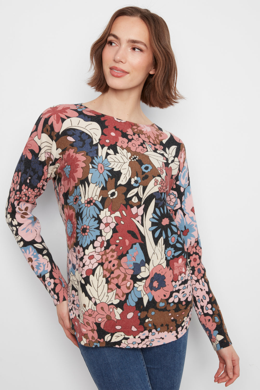 A woman wearing a long sleeve flower print sweater top standing in front of a white wall. 