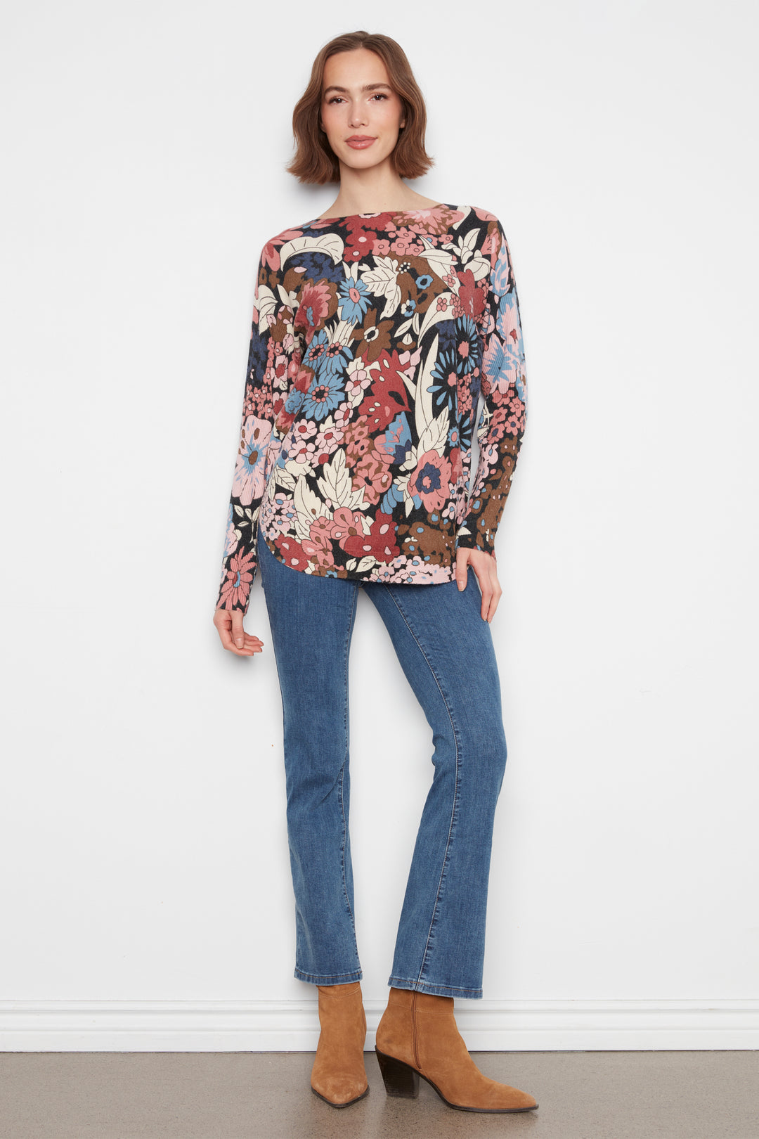 A woman wearing a long sleeve flower print sweater top standing in front of a white wall. 